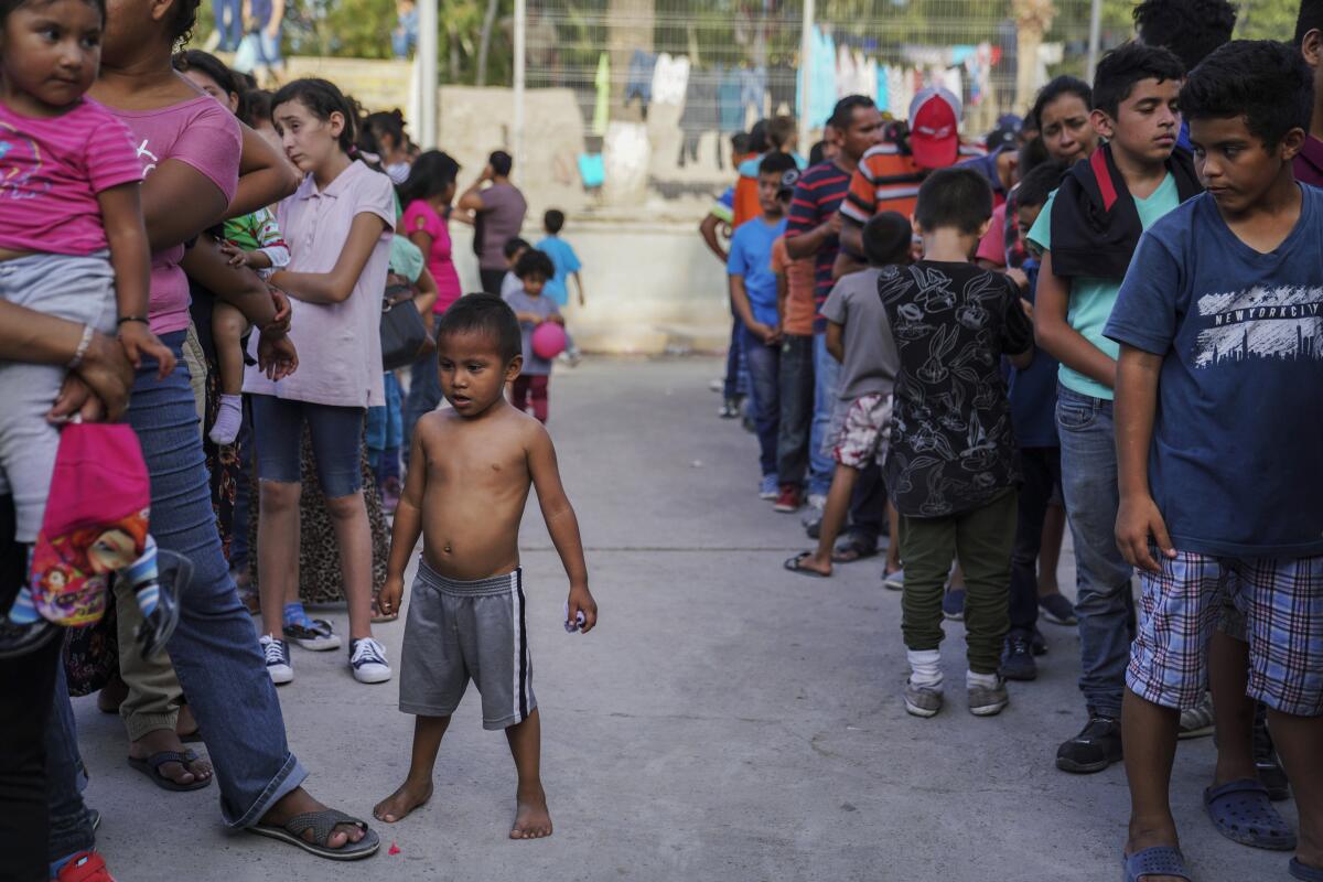 FILE - In this Aug. 30, 2019 file photo, migrants, many who were returned to Mexico under the Trump administration's "Remain in Mexico" program, wait in line to get a meal in an encampment near the Gateway International Bridge in Matamoros, Mexico. A federal appeals court has temporarily halted a major Trump administration policy to make asylum seekers wait in Mexico while their cases wind through U.S. immigration courts. A panel of the 9th U.S. Circuit Court of Appeals in San Francisco ruled Friday, Feb. 28, 2020, in a 2-1 vote to put on hold the policy that furthered President Donald Trump's asylum crackdown. (AP Photo/Veronica G. Cardenas, File)
