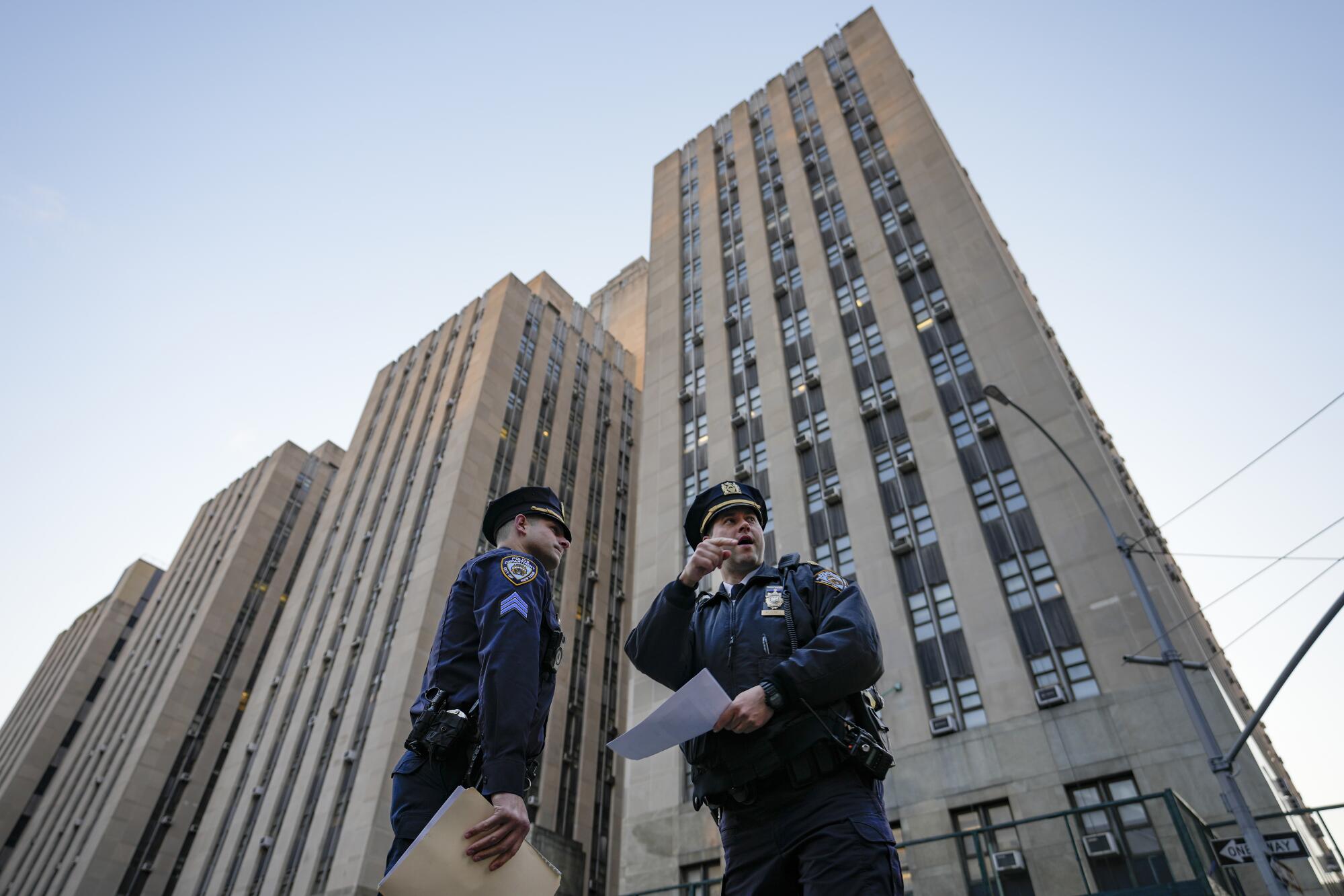 Framed by a low-angle view, two police officers secure the perimeter outside Manhattan Criminal Court.