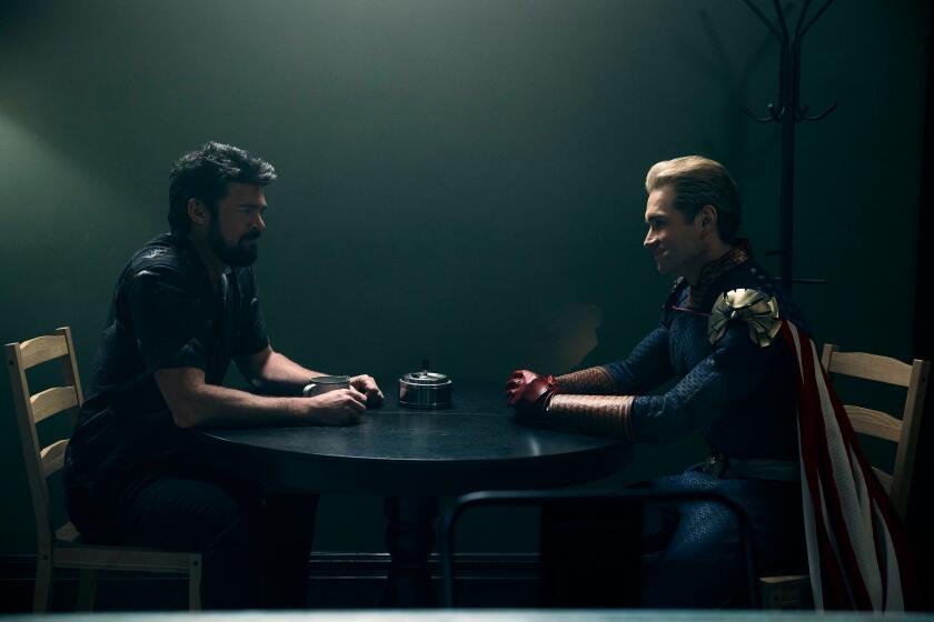 A regular human and a superhero who hate each other sit at a table (from the Amazon show "The Boys")