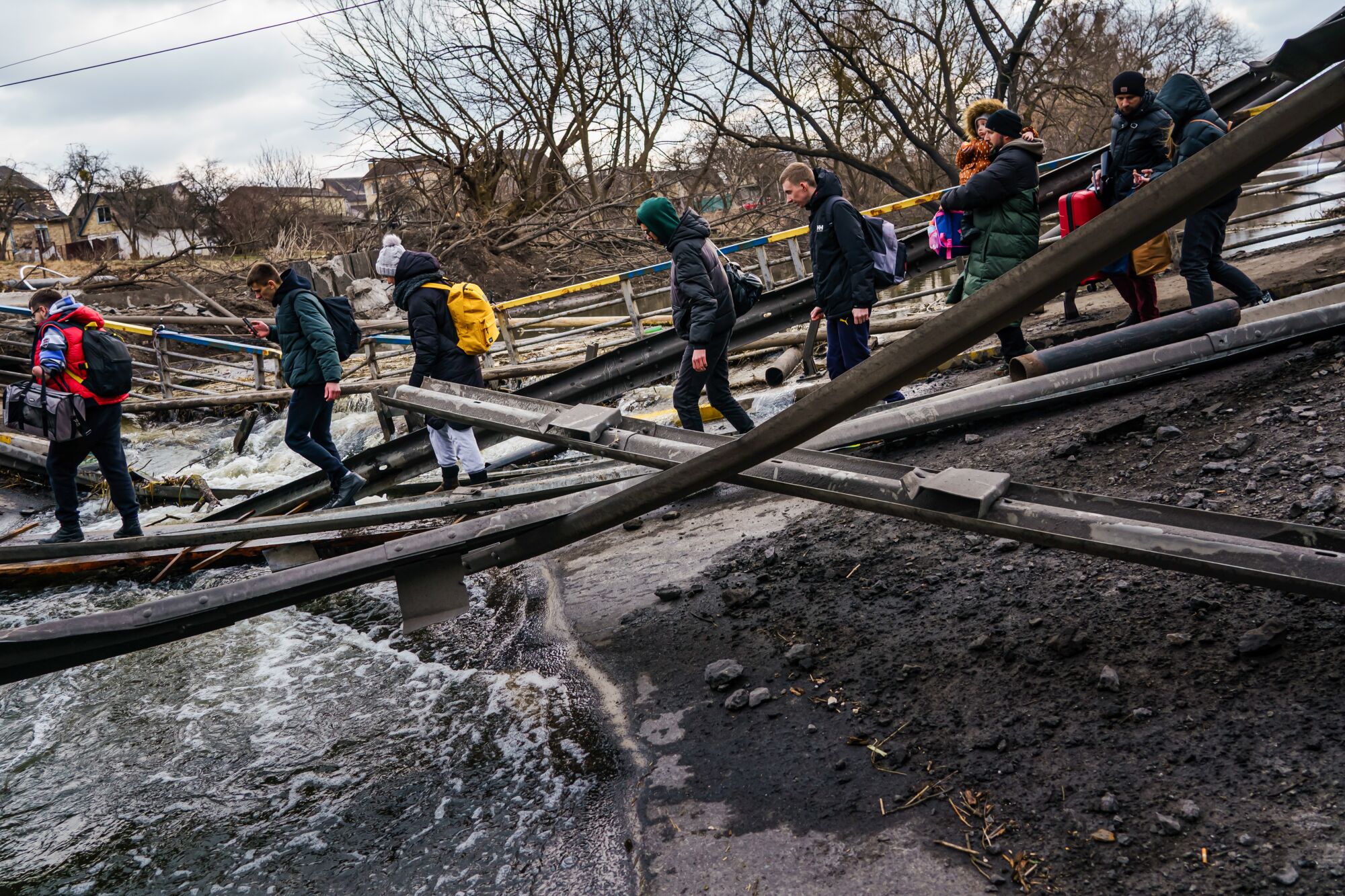 Civilians cross the Irpin River through the rubble of a destroyed bridge