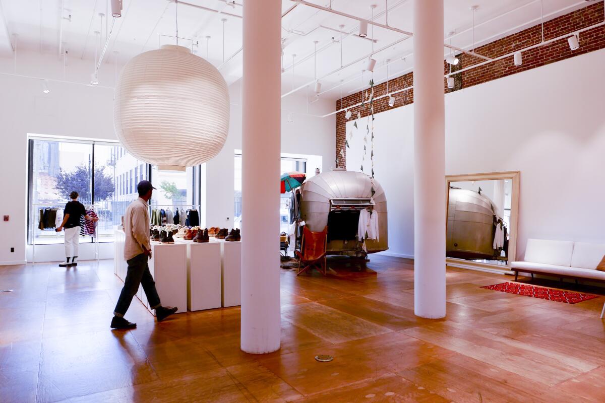 The interior of a store with sparse displays of clothing and shoes and an Airstream-style trailer