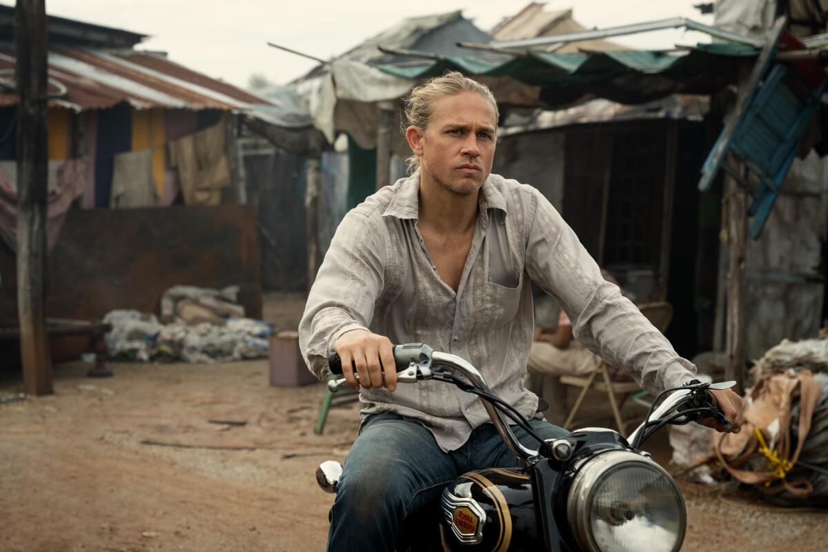 A man riding a motorbike through a slum.