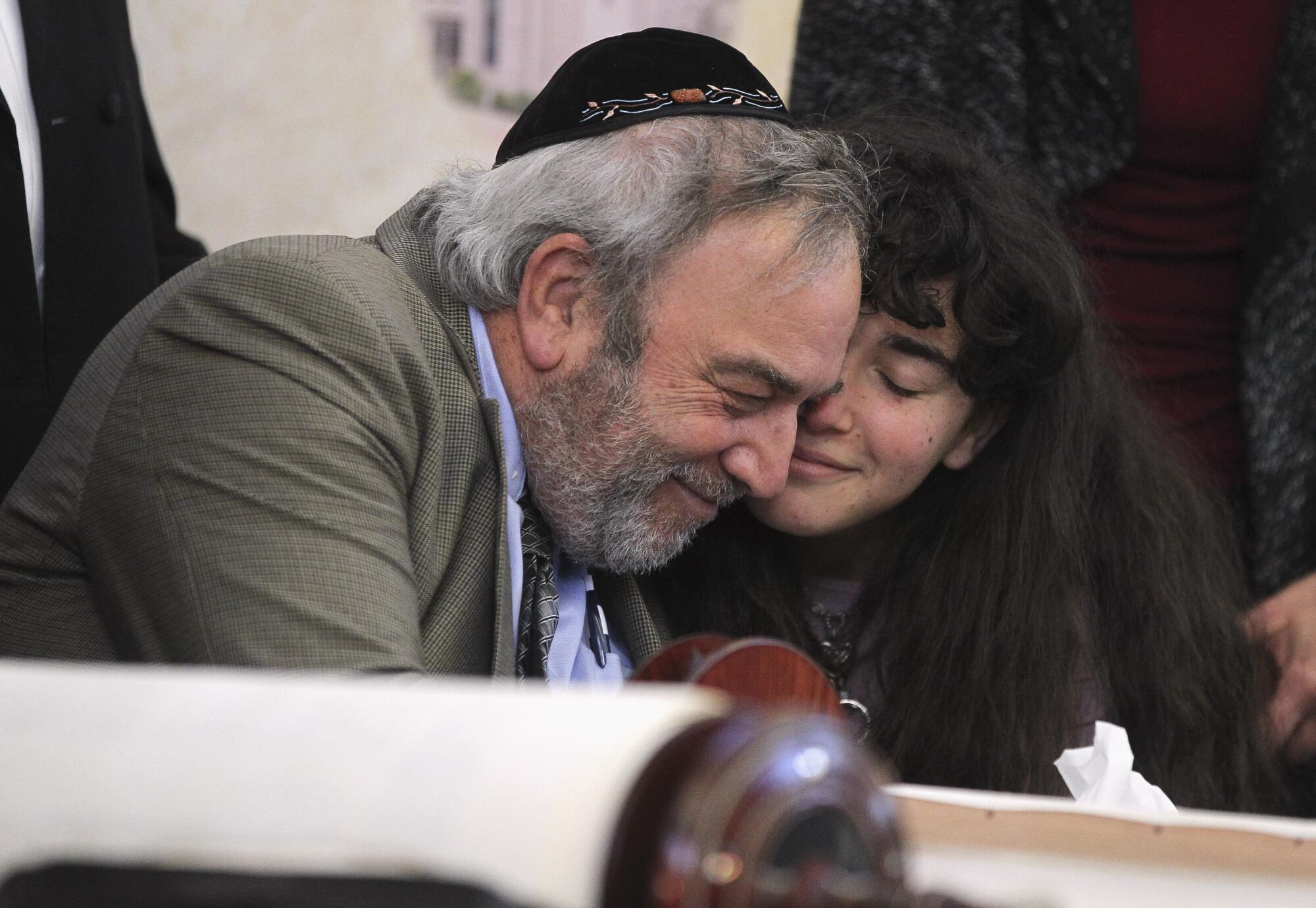 Howard Kaye, center, and his daughter Hannah Kaye hug after the final letter was inked into the new torah that's dedicated to wife and mother Lori Gilbert-Kaye, who was killed when a gunman attacked last April, during a celebration for the new torah at Chabad of Poway on Wednesday, May 22, 2019 in Poway, California.