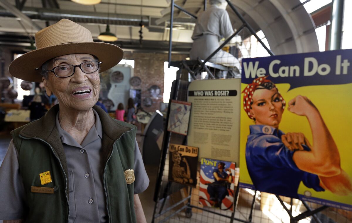 A smiling ranger stands back to a poster of Rosie the Riveter