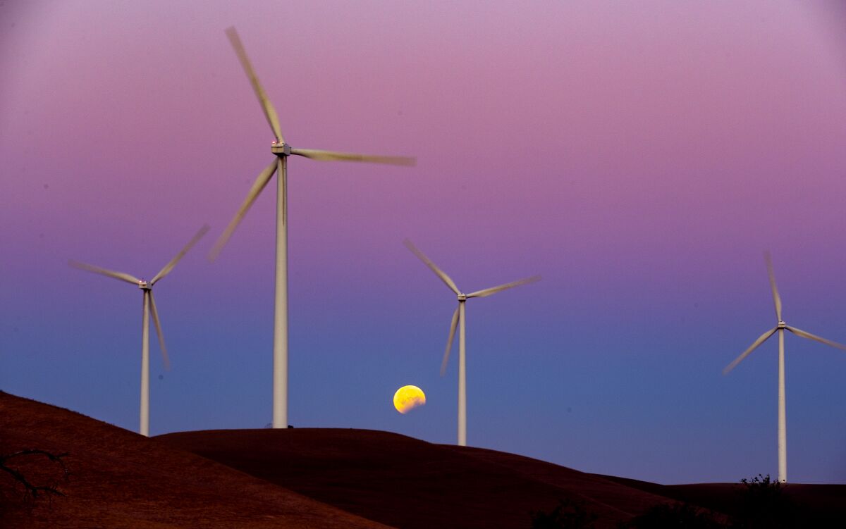 Wind turbines on a hillside with a moon in the background.