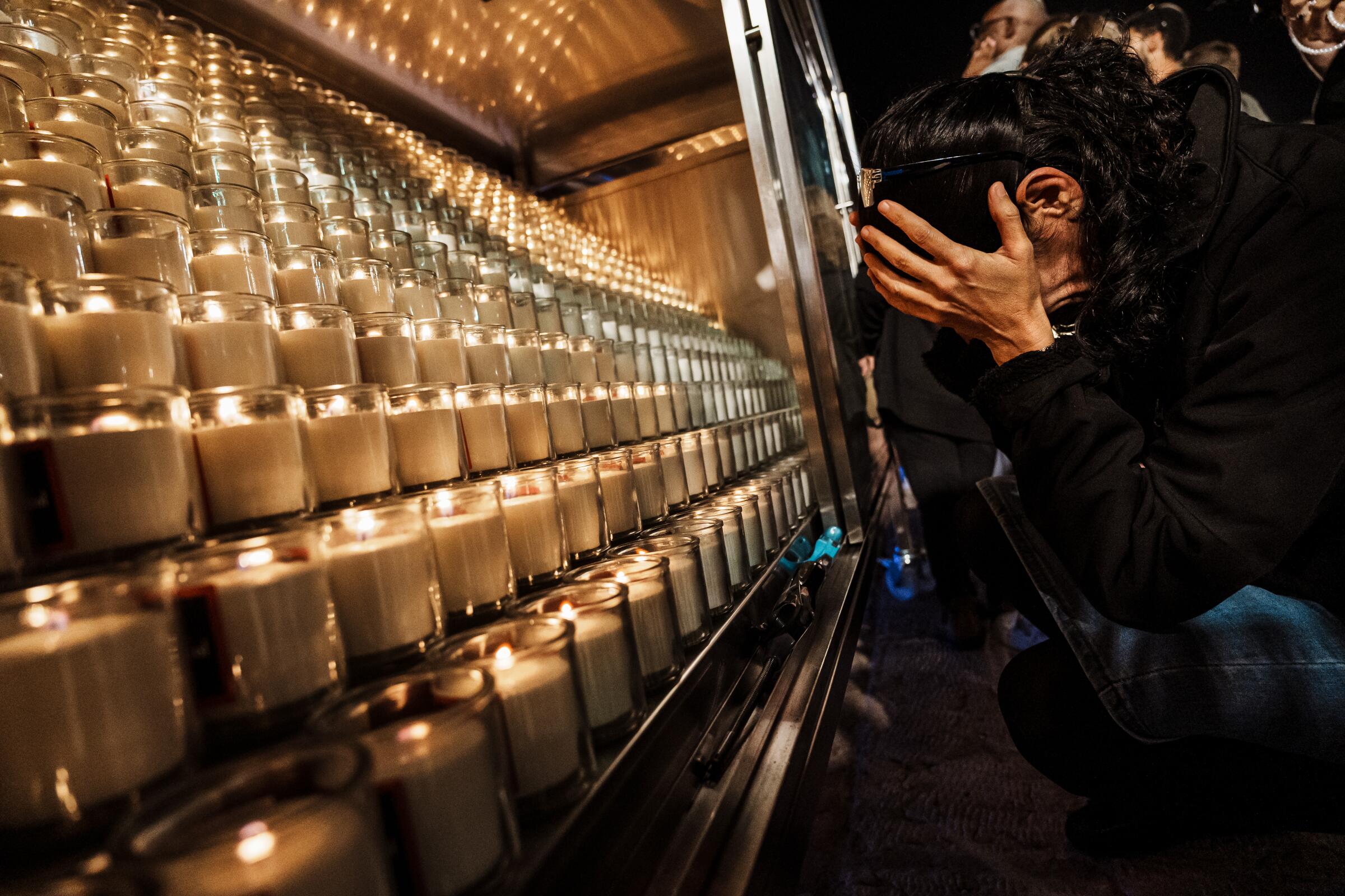 A woman weeps with her face in her hands in front of a display of candles 