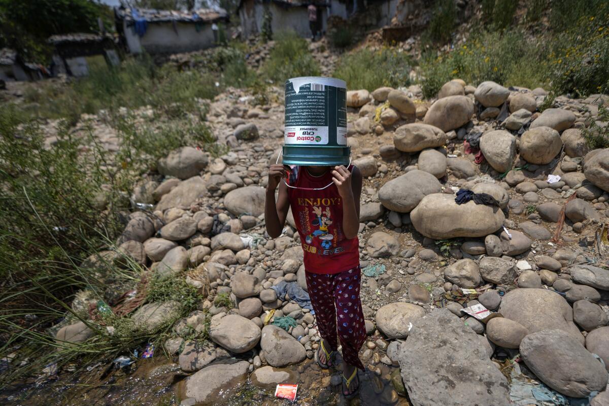 A girl covers her head with a bucket as she walks along a rocky path. 