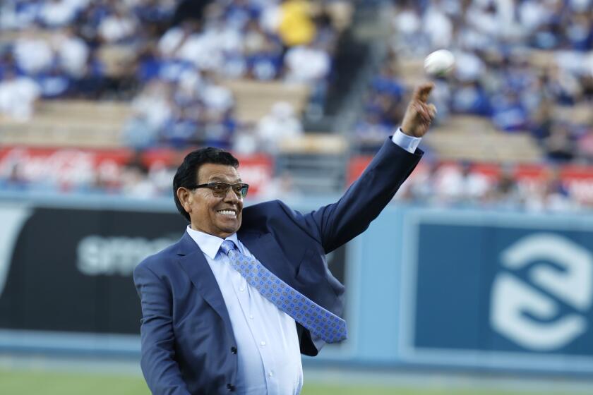 Fernando Valenzuela throws ceremonial first pitch at Dodger Stadium. He is wearing a blue grey suit with a white shirt.