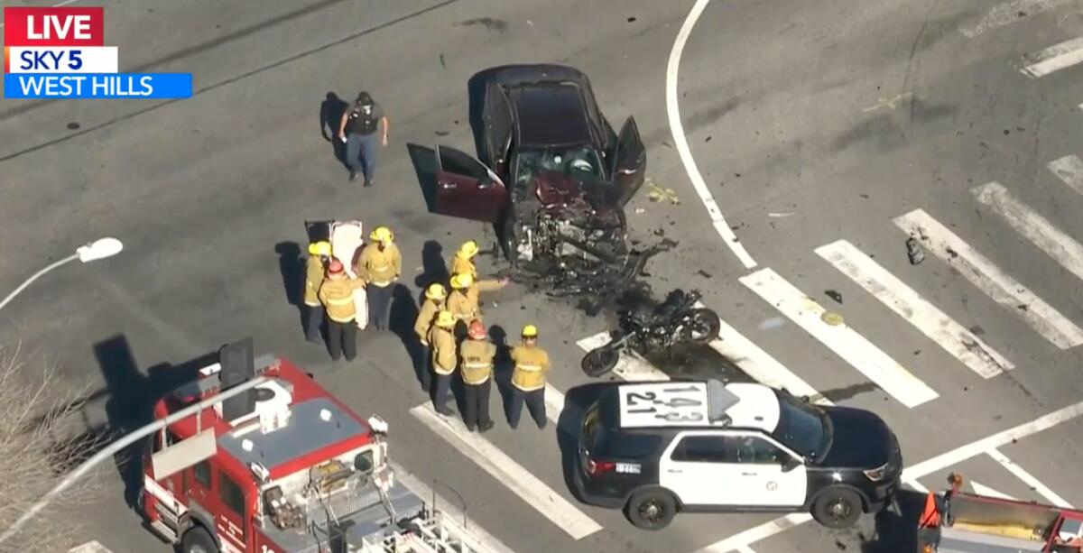 A damaged car and motorcycle sit in the road with emergency personnel around them.