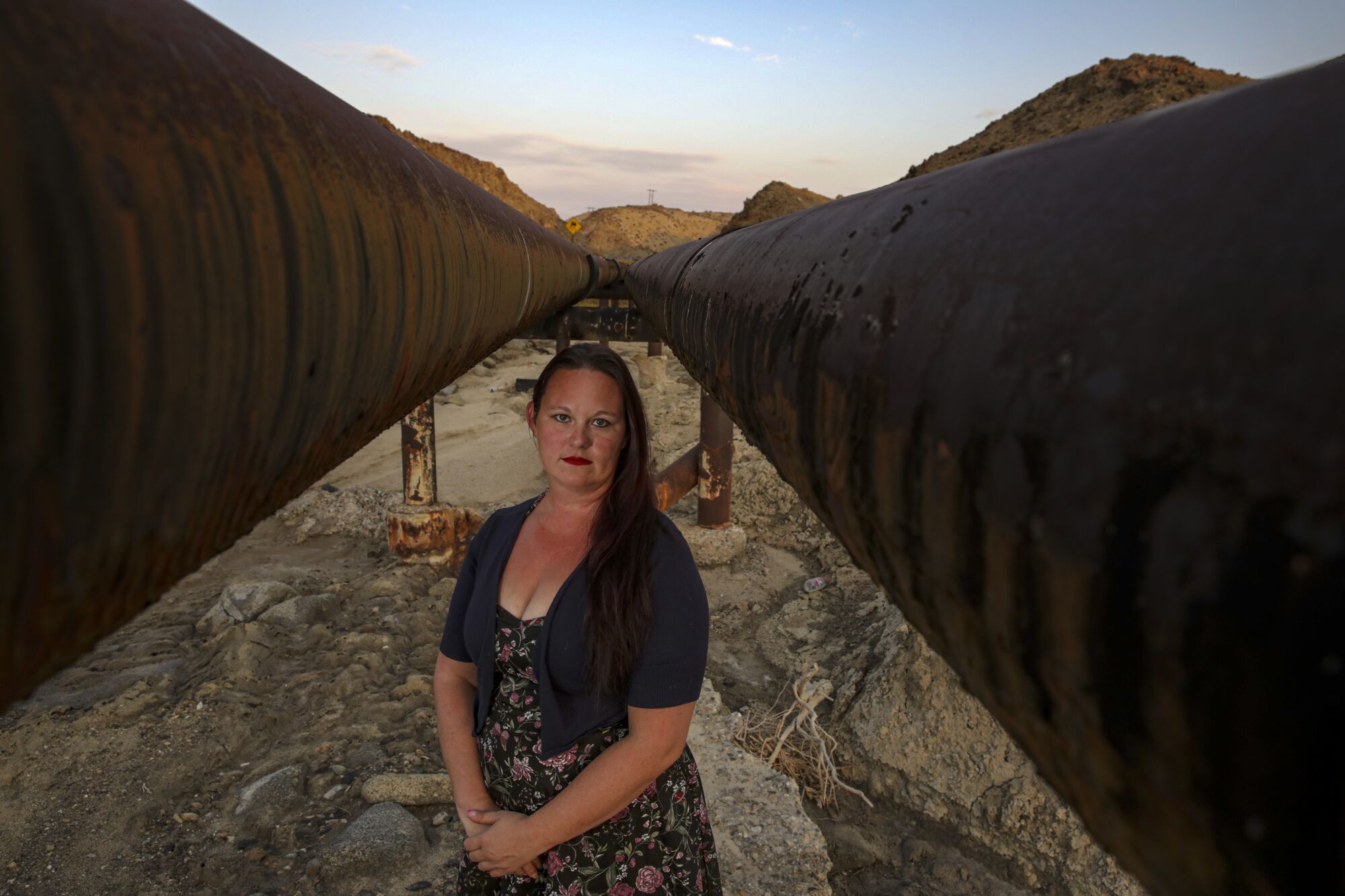 A woman stands between two large elevated water pipes
