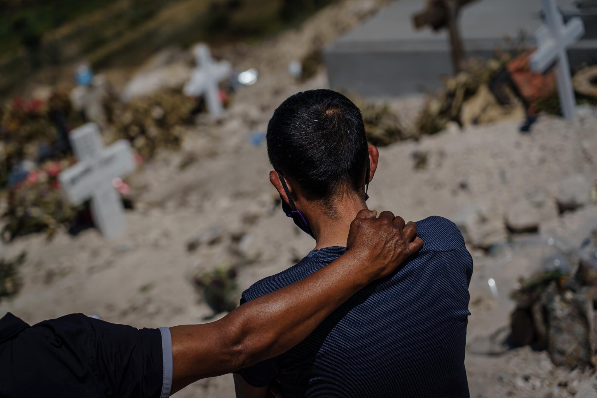 At Tijuana's Municipal Cemetery No. 13, Dominguez Hernandez consoles Fredy Villa Suerte Hernandez, right, as they mourn from a distance the death of Fredy's 49-year-old wife, Laura Moreno Sanchez, who died from COVID-19.