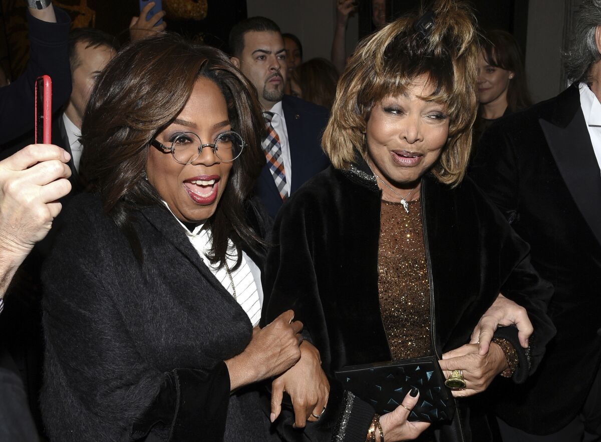 Oprah Winfrey and Tina Turner smile while standing together at a theater