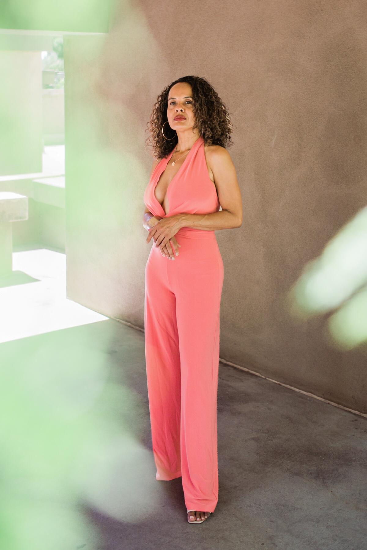 A full-length photo of a woman wearing a salmon-colored sleeveless jumpsuit.