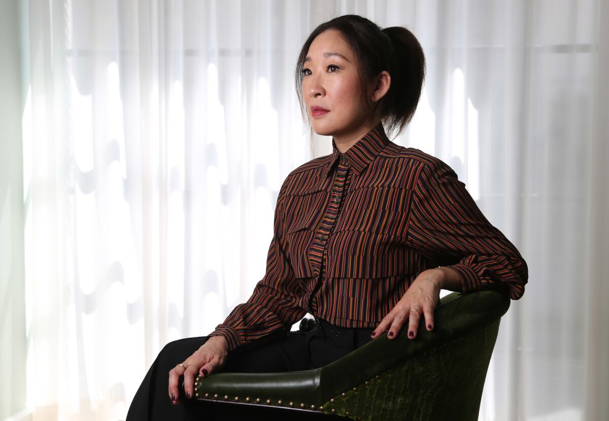 Sandra Oh, seated, in a red striped button-down shirt