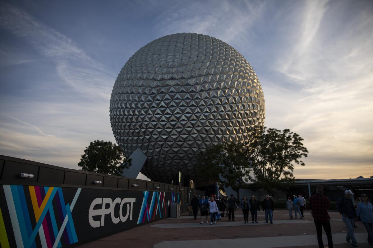 A golf-ball-like structure near a wall with the word EPCOT and people standing in front