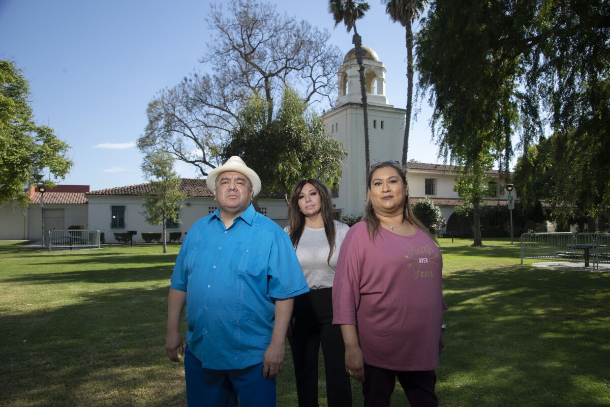 Three people stand on a lawn in front of a domed building.
