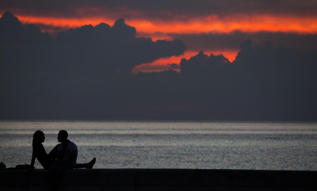 The setting sun lights up the sky over the Straits of Florida as a couple enjoy an evening on the Malecon in Havana.