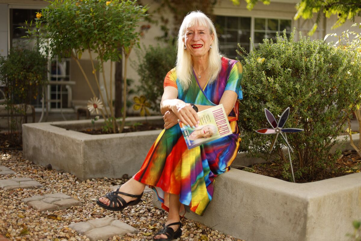 Mary Ann Horton, seated outdoors in multi-colored dress, holding a copy of her memoir