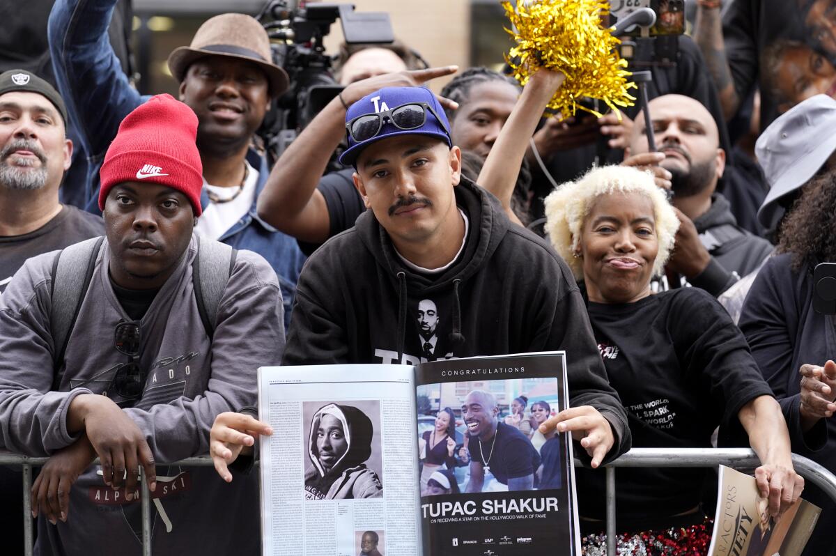 A fan holds up an image from a book of late rapper and actor Tupac Shakur surrounded by a crowd of others