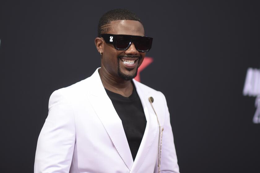A man smiling in sunglasses and a white suit