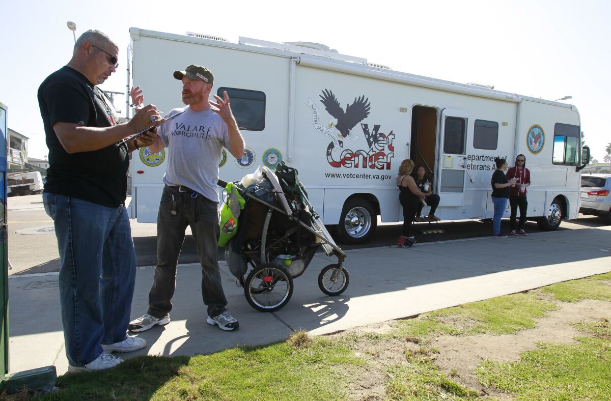 Veteran outreach specialist Bo Gonzales Jr., left, takes down information as he talks to homeless Navy veteran Patrick O'Connor while near the RV, background, that a group of veteran outreach workers use to go to where the homeless veterans are in Ocean Beach.