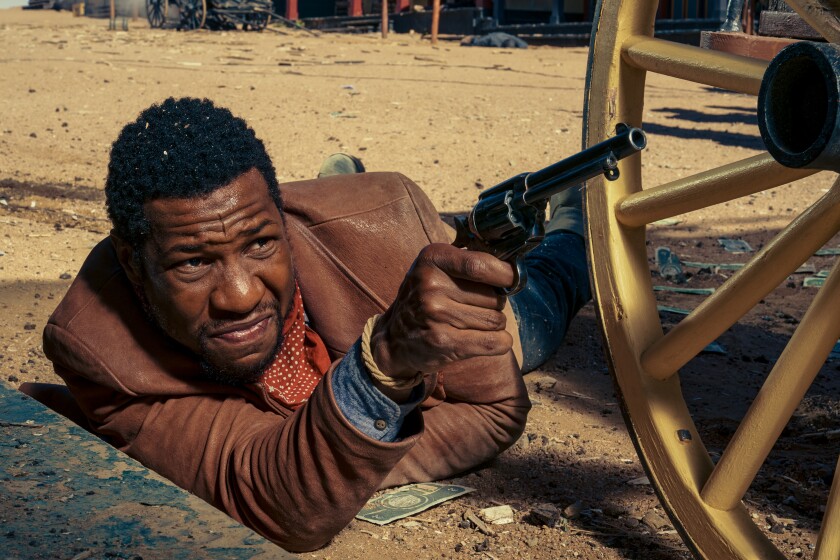 A man lying down squints as he points a gun.