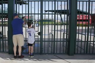FILE - Cubs fans take photos through the locked gates at Sloan Park, the spring training site of the Chicago Cubs.