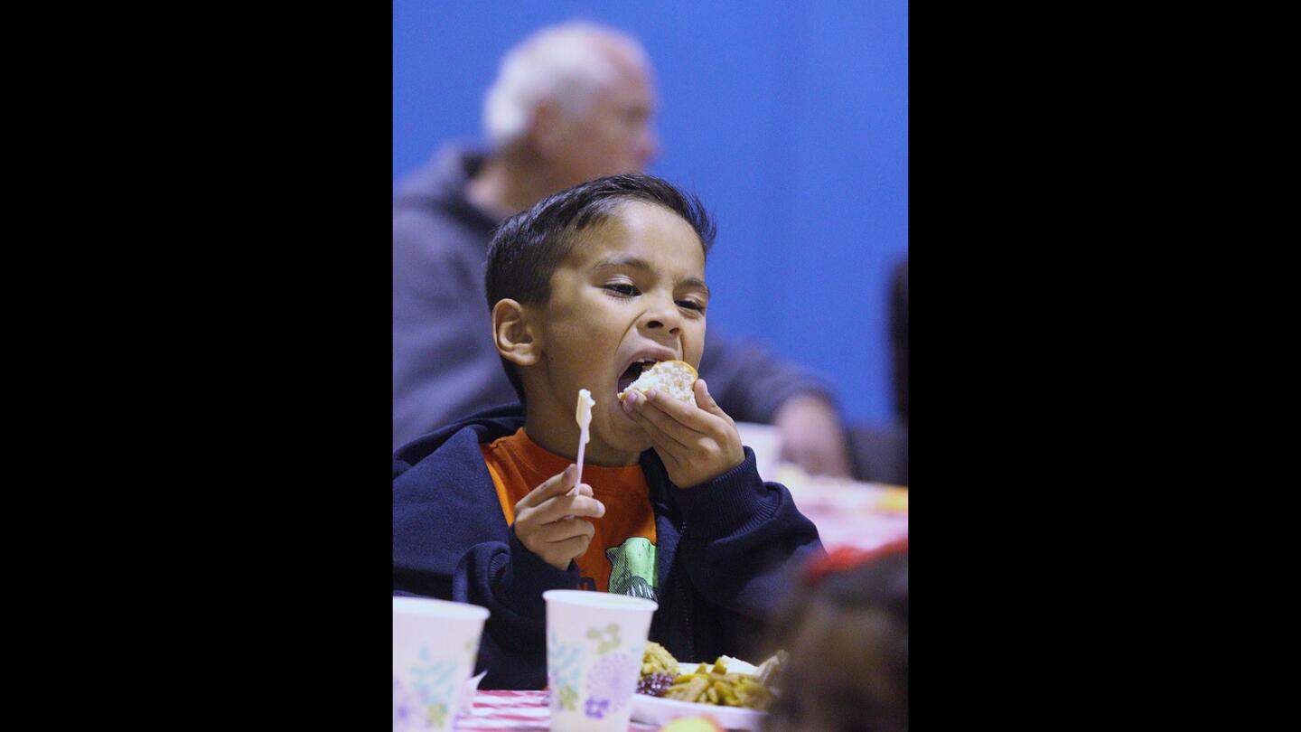 Matthew Martinez, 8, of Glendale, takes a big bite of a dinner roll at the Salvation Army Glendale Corps and Community Center Thanksgiving dinner in Glendale on Thursday, Nov. 26, 2015.