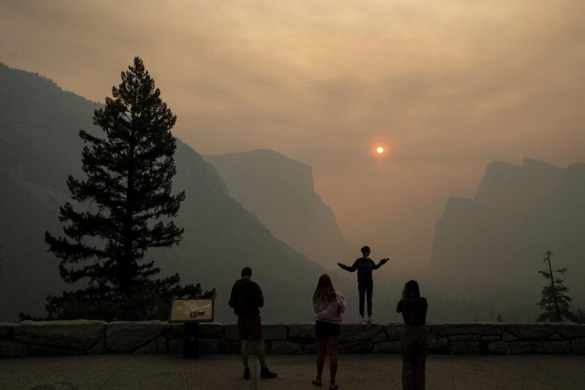 FILE - In this July 25, 2018 file photo, Hannah Whyatt poses for a friend's photo as smoke from the Ferguson fire fills Yosemite Valley in Yosemite National Park, Calif. Yosemite National Park could reopen its scenic valley and other areas Monday, Aug. 6, 2018, if conditions improve after a 12-day closure due to nearby wildfires. The parkâs iconic cliffs have been shrouded in so much smoke that the air quality in Yosemite is currently worse than Beijing. (AP Photo/Noah Berger, File)