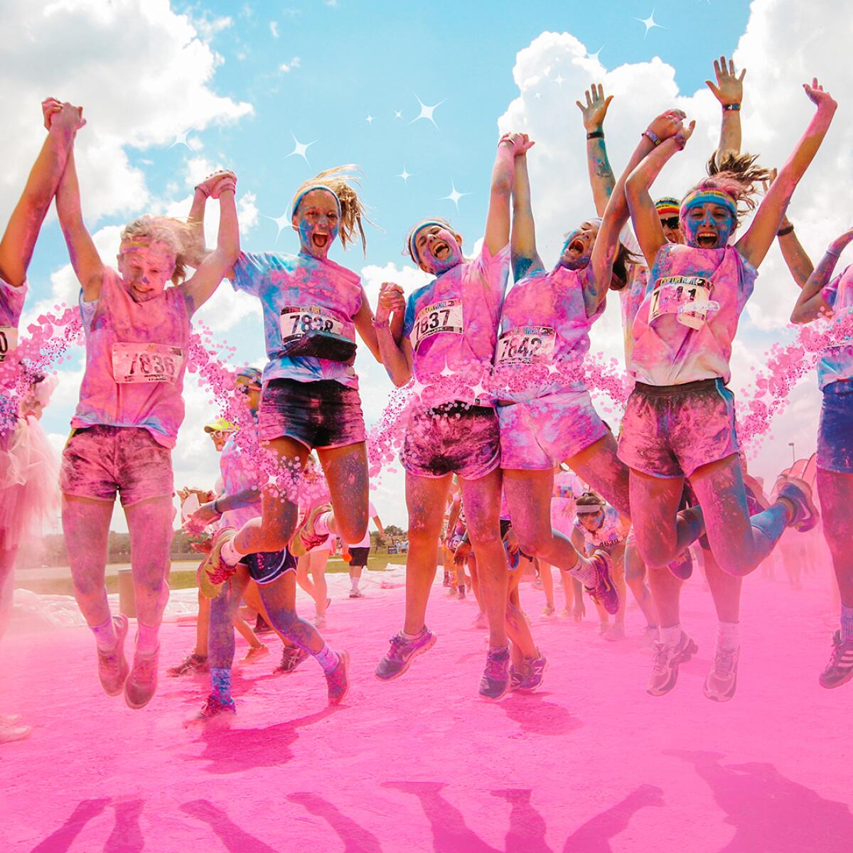 A group of people covered in pink chalk jump in the air.