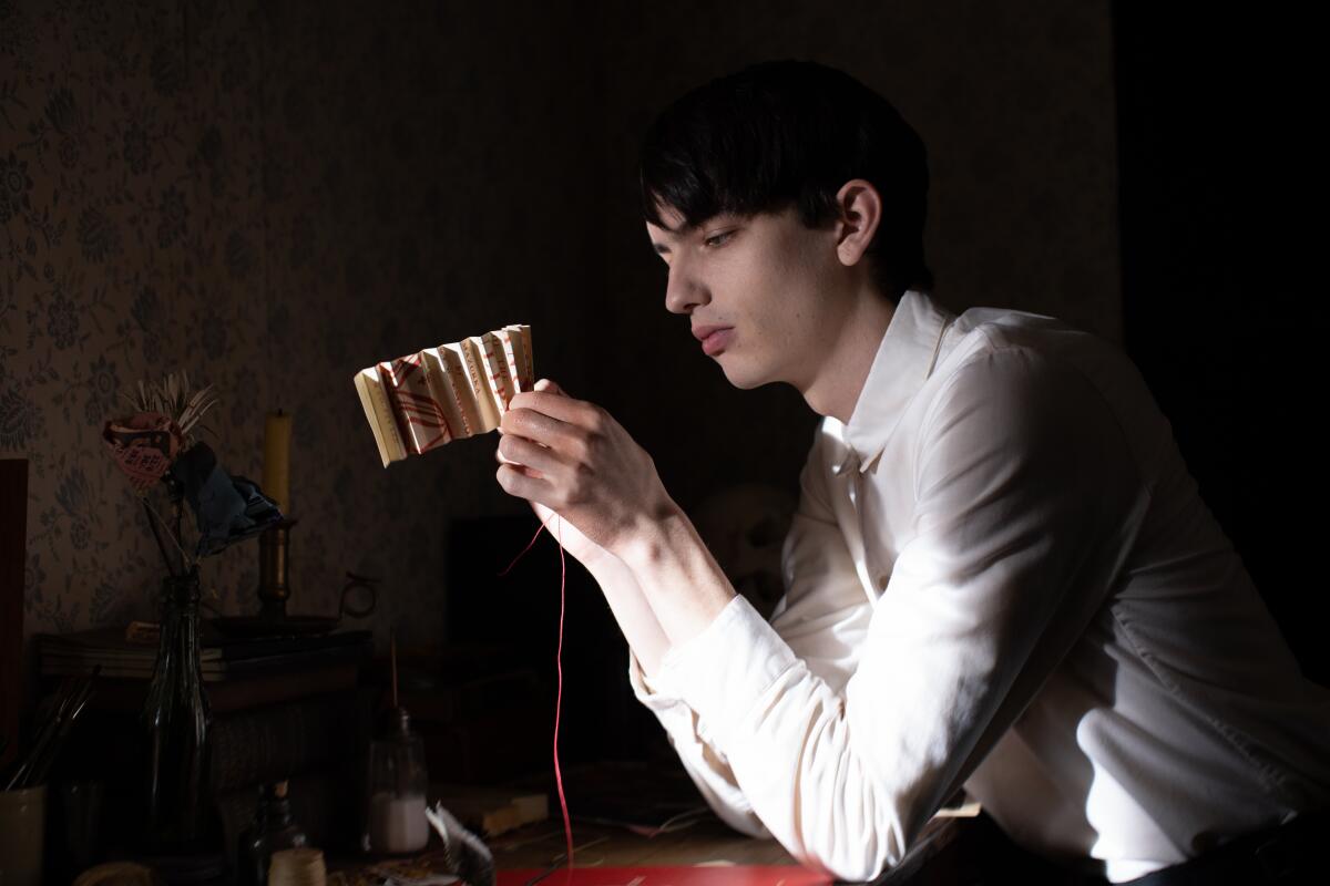 A dark-haired man in a white shirt makes paper flowers in "The Power of the Dog."