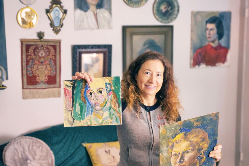 With a portrait in one hand and older art in the other, Sheree Perelman in front of a gallery wall of vintage portraits.