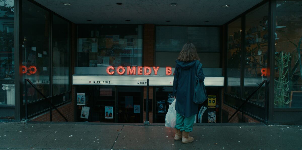 A woman stands outside a comedy club and looks at the marquee.
