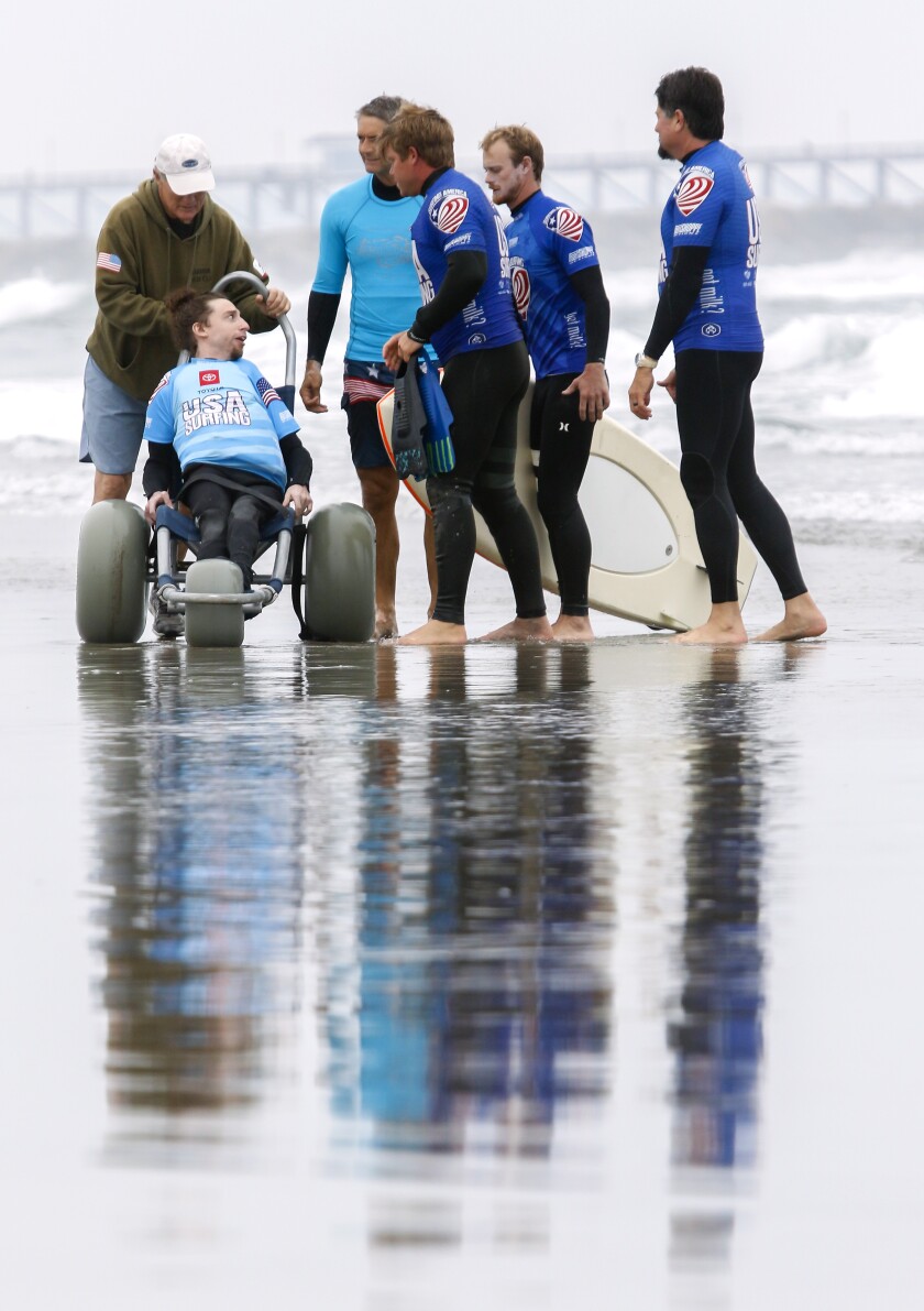 Surfer Dylan Hronec talks with his team before competing in his prone assist contest at the USA Surfing Adaptive Surfing Championship at Oceanside Harbor North Jetty.  