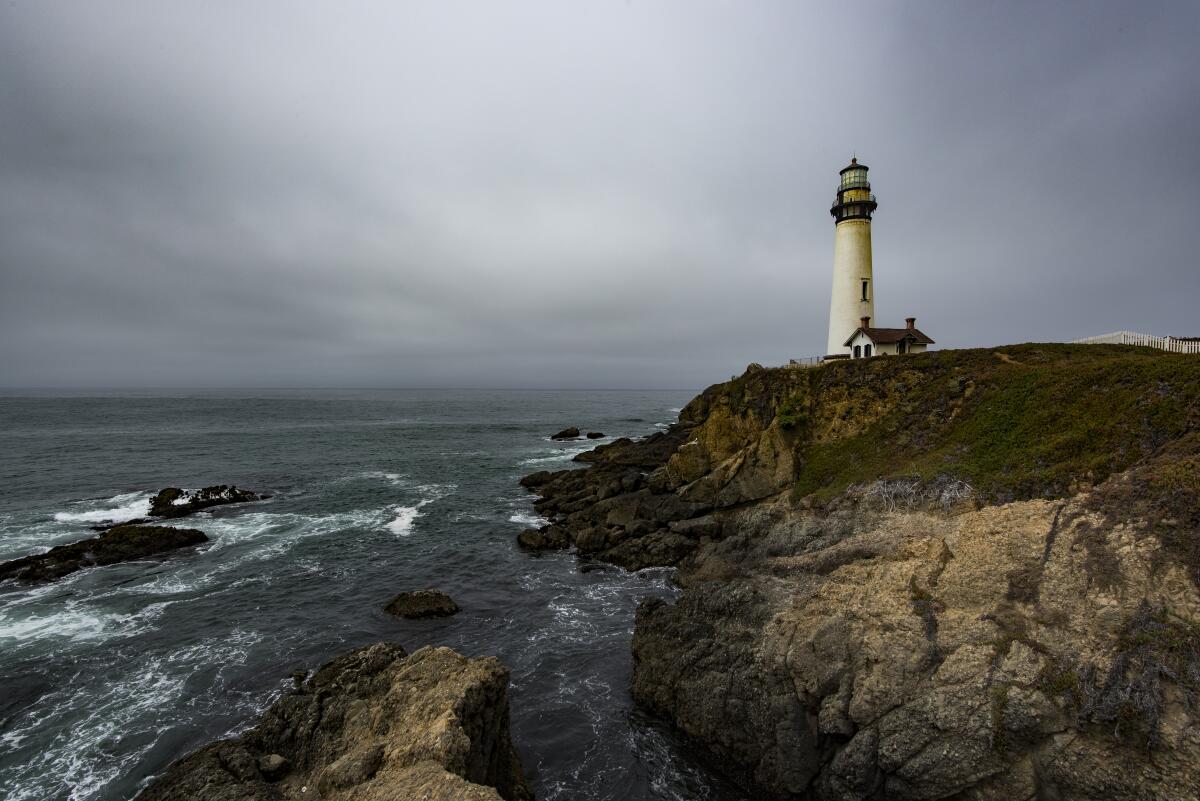 A lighthouse high on a cliff above whitecapped sea under stormy gray sky