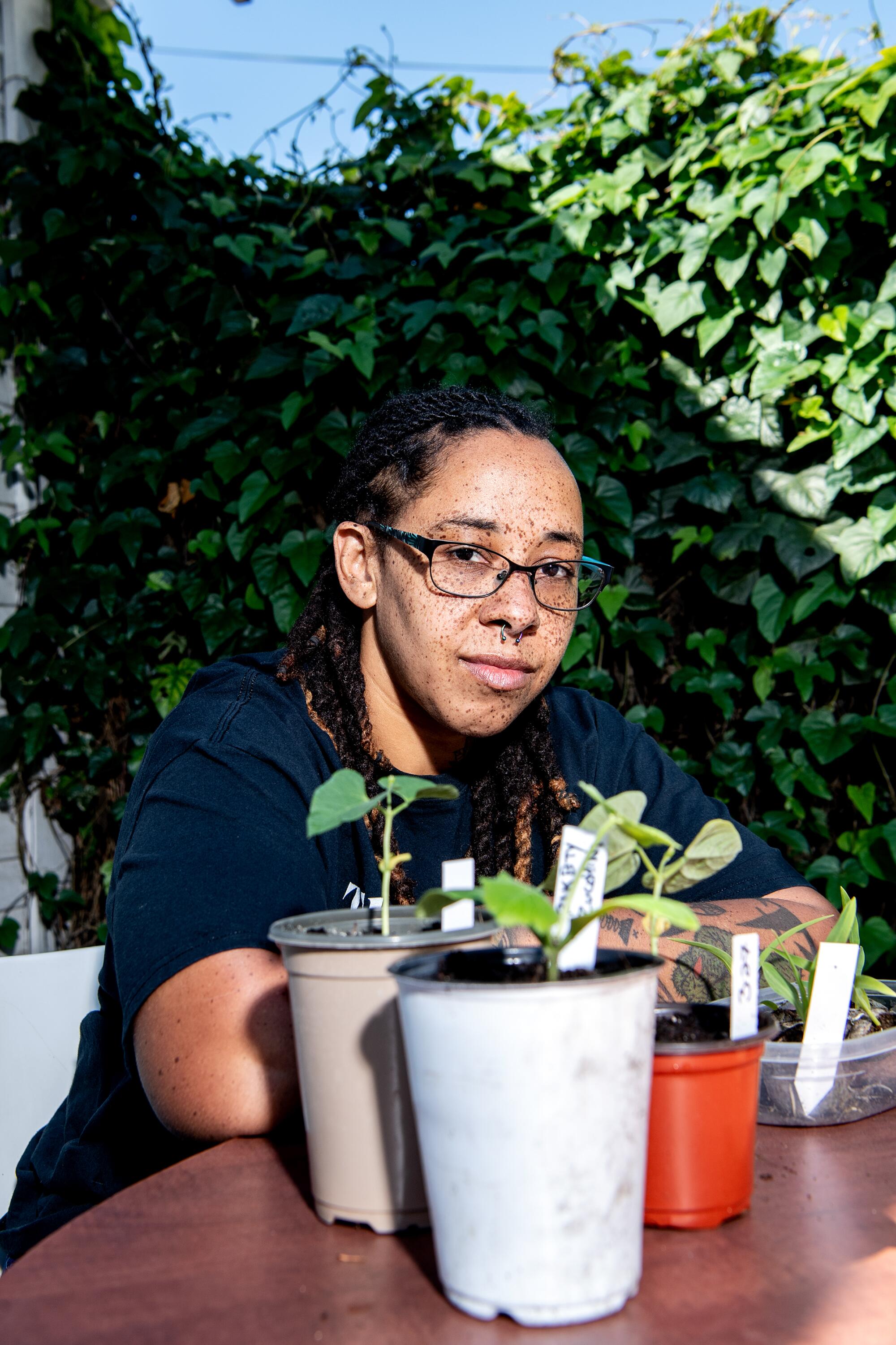 A woman sits behind an array of potted plants.
