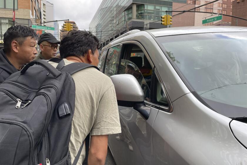 Wang Gang, de 36 a?os, delante, un migrante chino, habla con el conductor de un coche junto a otras personas mientras intentan conseguir un trabajo jornalero en la construcción o en otro oficio en el barrio de Flushing, en el barrio neoyorquino de Queens, el 3 de mayo de 2024. (AP Foto/Fu Ting)