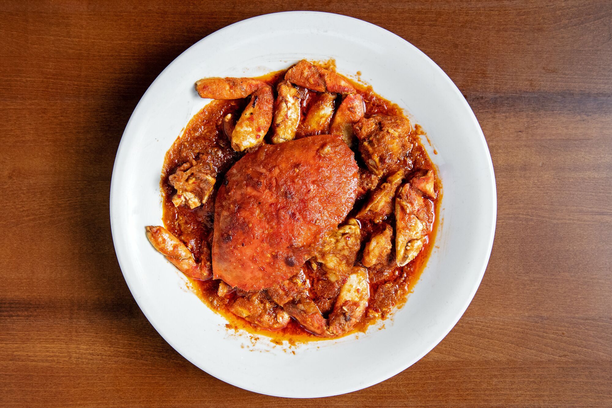 Crab covered in red sauce served on a white plate.