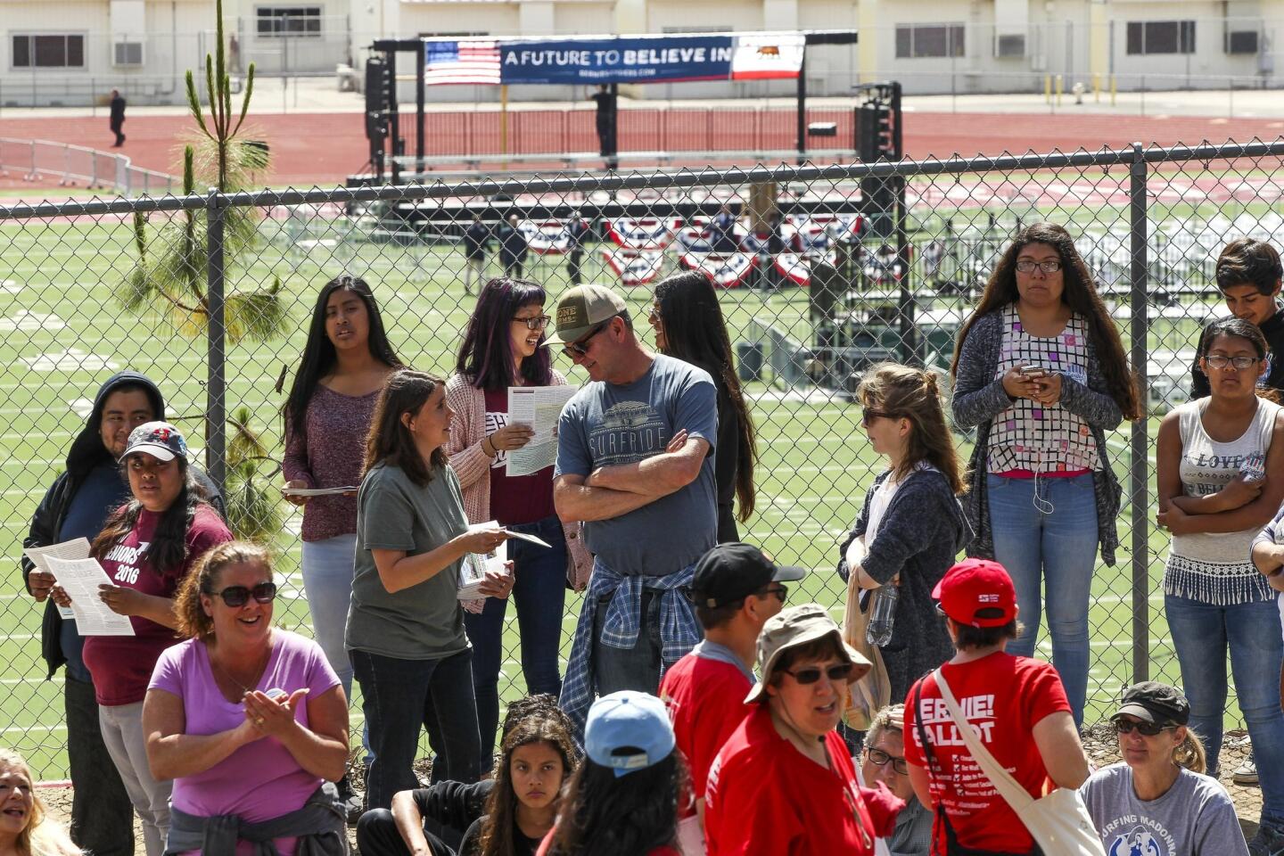 As the stage is prepared in the background, people stand in line as the wait to see Democratic presidential candidate Bernie Sanders.