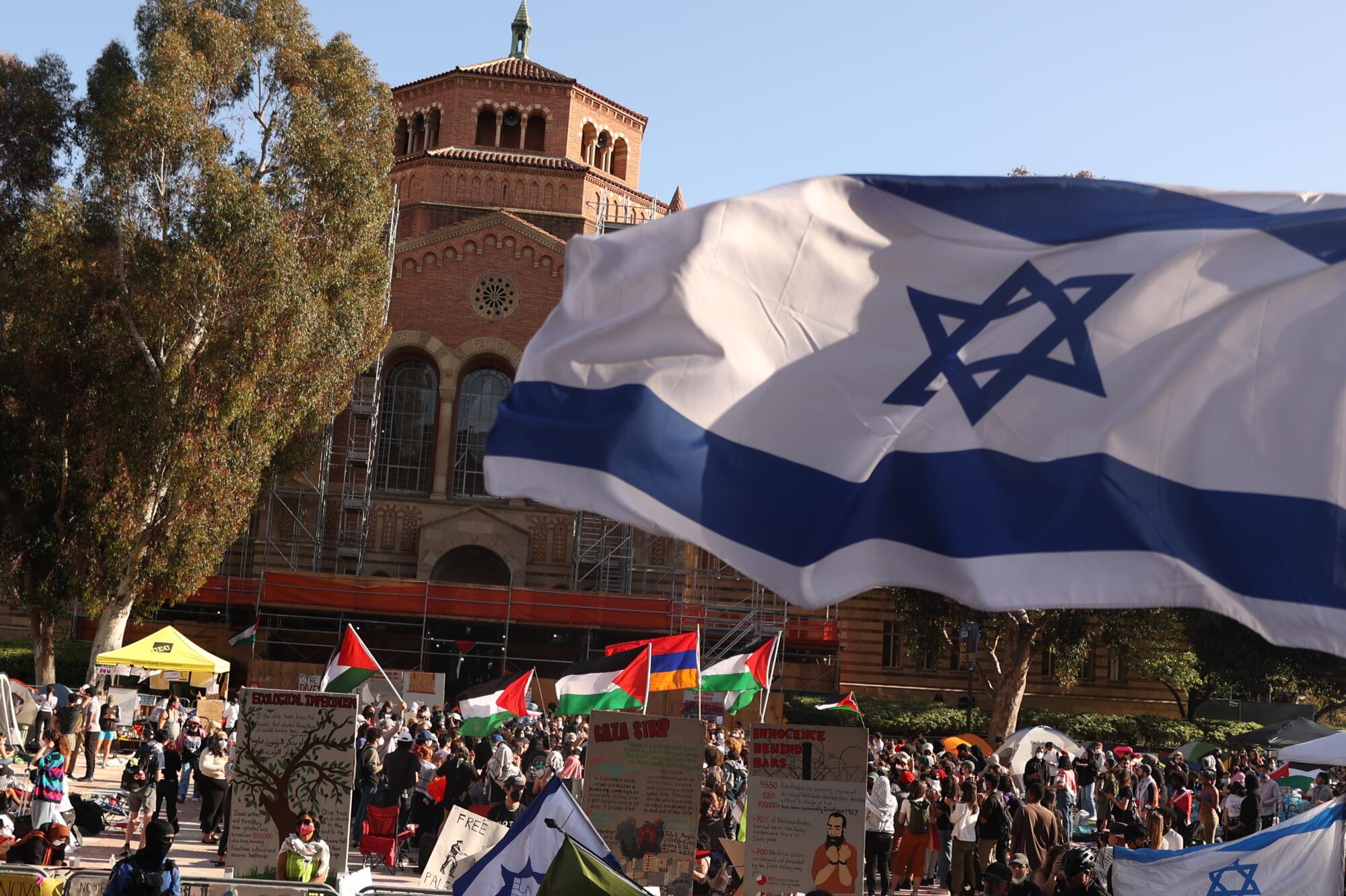 An Israel flag waves high near a pro-Palestine protest that has students in an encampment outside of Royce Hal
