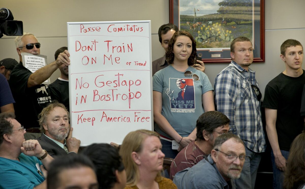 Bob Welch, standing at left, and Jim Dillon, hold a sign at a public hearing last April about the Jade Helm 15 military training exercise in Bastrop, Texas.