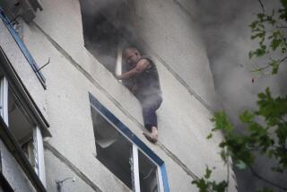 A man straddles a window opening of his  burning apartment.