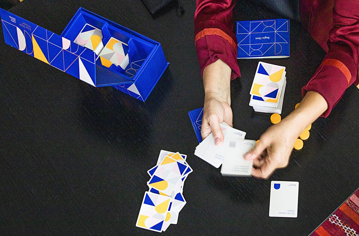 Hands hold cards above a table holding more cards and a box