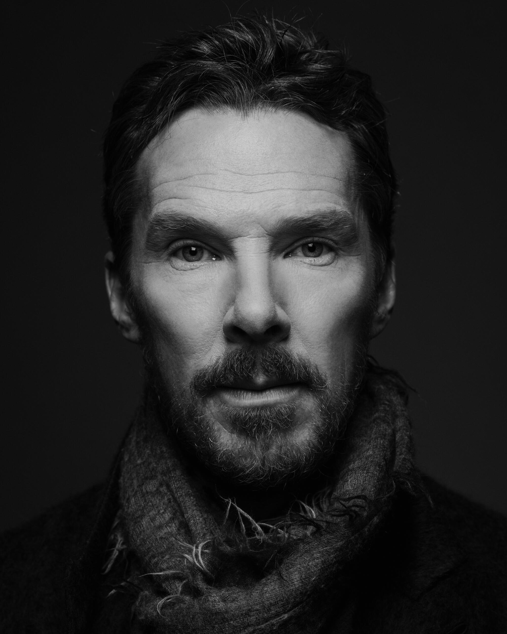 A portrait of Benedict Cumberbatch in dark jacket and scarf, his hand to his chest.