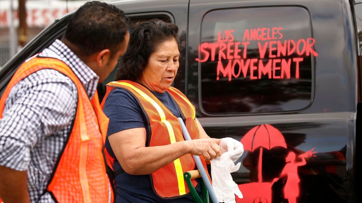 Street vendor Rosa Alaman, right, and Eloy Hernandez join other street vendors and supporters as they use brooms and trash bags to clean the street median at the intersection of Tobias Avenue and Parthenia Street in Panorama City.