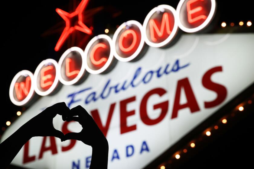 Ragne Domaas, of Norway, makes a heart symbol with her hands as her friend takes a photo Friday, Oct. 6, 2017, at Las Vegas' famous sign near a makeshift memorial for victims of a mass shooting in Las Vegas. Stephen Paddock opened fire on an outdoor music concert on Sunday killing dozens and injuring hundreds. (AP Photo/John Locher)
