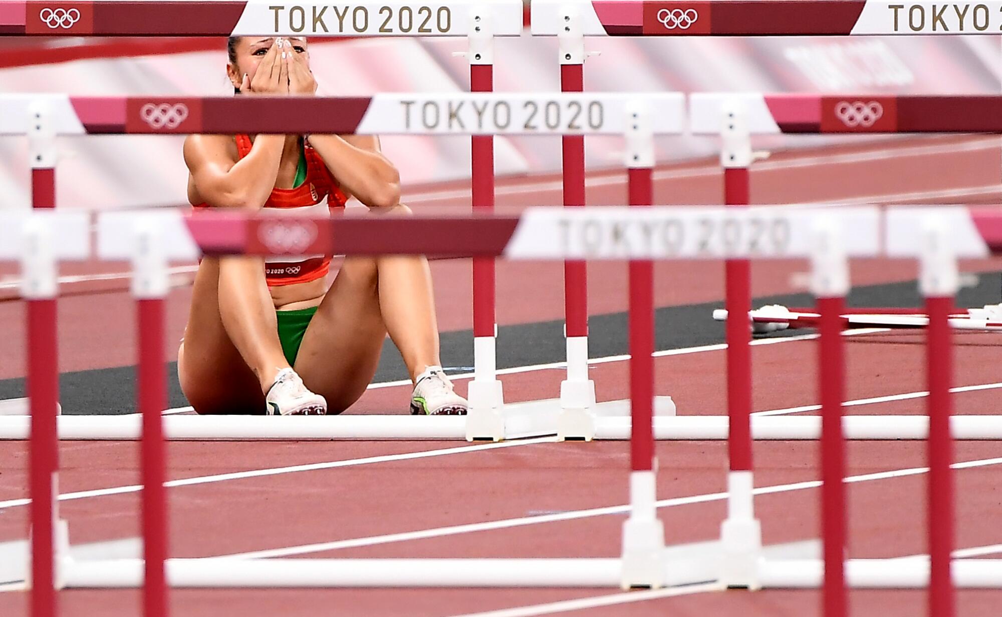 Luca Kozak sits on the track, holding her hands to her face.
