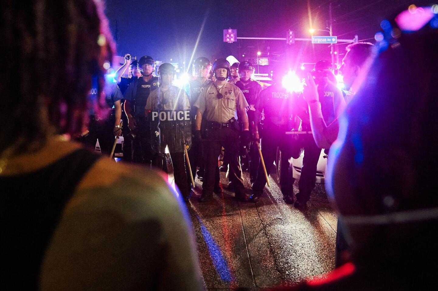 St. Louis County police and Missouri State Highway Patrol troopers stand guard as protesters (foreground) march on West Florissant Avenue in Ferguson, Mo., on Aug. 9, 2015.