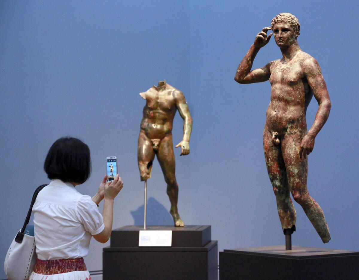 A woman takes a cellphone photo of a statue in a museum