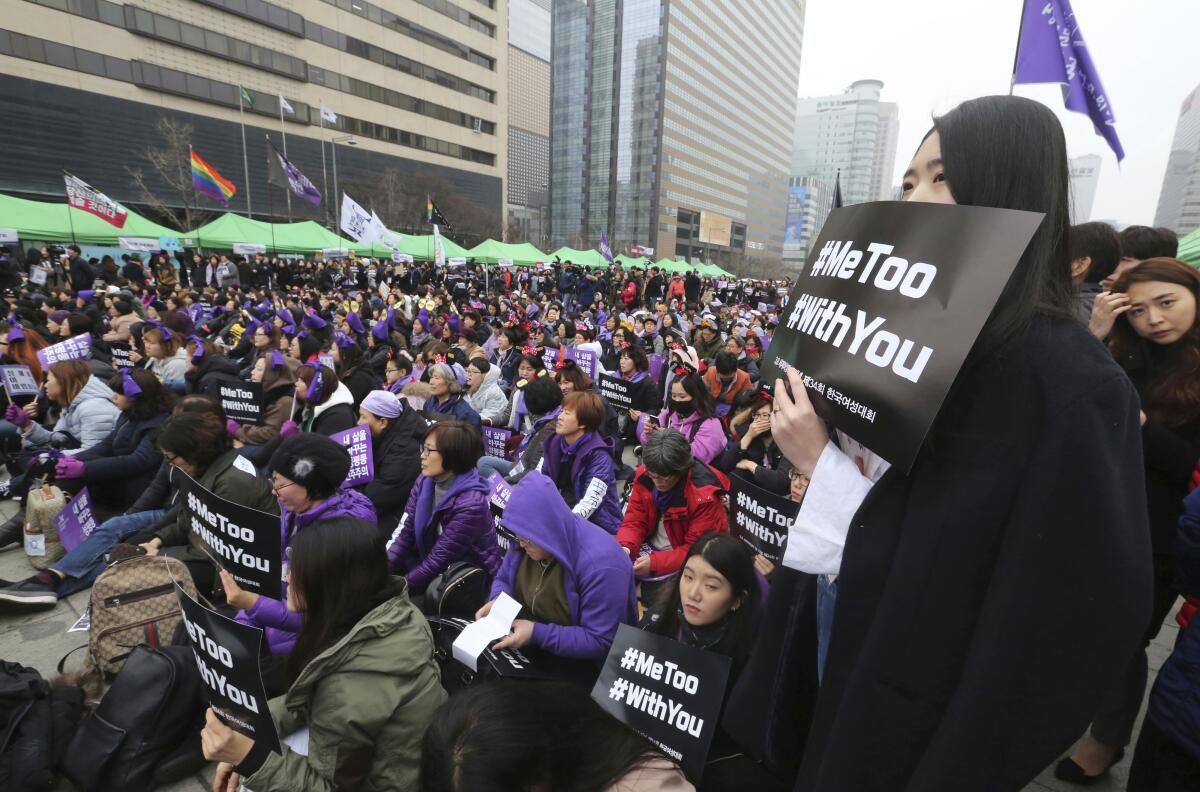 A huge crowd of women, some holding #MeToo signs, gathers near buildings